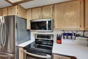 Kitchen featuring appliances with stainless steel finishes, light countertops, and light brown cabinetry