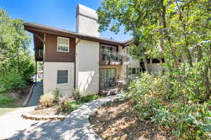 Rear view of property with a balcony, stucco siding, and a chimney