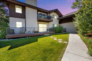 Back of property featuring a balcony, a lawn, stucco siding, and a wooden deck