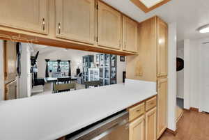 Kitchen featuring light brown cabinetry, a desk, light countertops, stainless steel dishwasher, and open floor plan