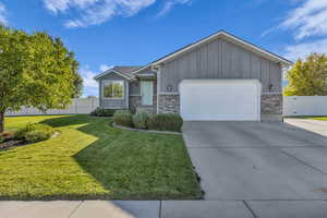View of front of home featuring board and batten siding, an attached garage, driveway, brick siding, and a gate
