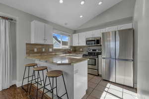 Kitchen featuring appliances with stainless steel finishes, vaulted ceiling, a breakfast bar area, white cabinets, and a peninsula