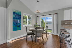 Dining space with lofted ceiling, dark wood finished floors, healthy amount of natural light, and a chandelier