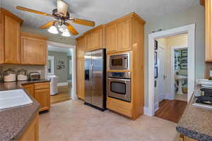 Kitchen with stainless steel appliances, light tile patterned floors, a ceiling fan, light brown cabinetry, and a textured ceiling