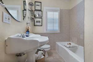 Bathroom featuring tile patterned floors, a textured wall, tile walls, and washtub / shower combination