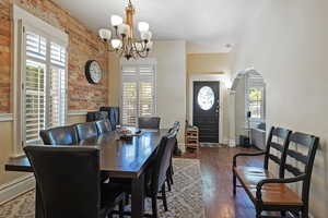 Dining area with brick wall, dark wood finished floors, arched walkways, and a chandelier