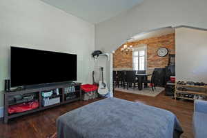 Bedroom featuring dark wood-style floors, a chandelier, brick wall, and arched walkways