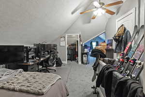 Bedroom featuring light colored carpet, a walk in closet, a textured ceiling, lofted ceiling, and ceiling fan