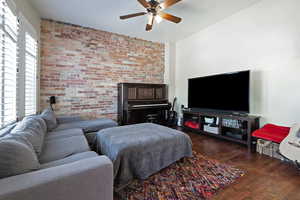 Living area with brick wall, dark wood-type flooring, and ceiling fan