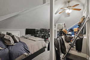 Bedroom featuring a textured ceiling, lofted ceiling, and a ceiling fan