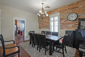 Dining room featuring dark wood-style floors, brick wall, and a chandelier