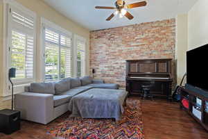 Living room featuring brick wall, dark wood-type flooring, and ceiling fan