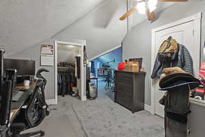 Carpeted office featuring a textured ceiling, lofted ceiling, and a ceiling fan