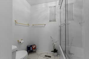 Full bath featuring light marble finish floors and shower / bath combination with glass door