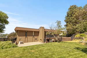 Rear view of property featuring brick siding, a wooden deck, a chimney, and a yard