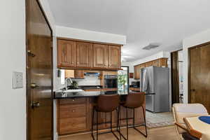 Kitchen featuring a peninsula, brown cabinets, black appliances, light wood finished floors, and a breakfast bar