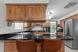 Kitchen featuring freestanding refrigerator, dark stone countertops, a peninsula, brown cabinets, and black oven