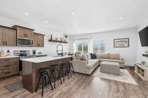 Kitchen featuring appliances with stainless steel finishes, an island with sink, a kitchen breakfast bar, dark wood-style flooring, and recessed lighting