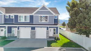 View of front of property with driveway, stone siding, an attached garage, and private side yard
