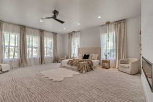 Carpeted bedroom featuring a glass covered fireplace, ceiling fan, and recessed lighting