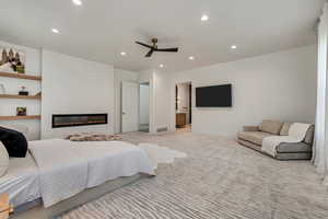 Carpeted bedroom featuring a glass covered fireplace, recessed lighting, a ceiling fan, and ensuite bathroom