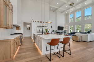 Kitchen with glass insert cabinets, open floor plan, beamed ceiling, stainless steel stove, and light wood-style flooring