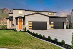 Modern home with a garage, concrete driveway, a lawn, and stone siding
