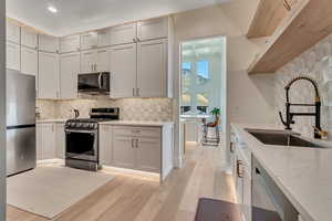 Kitchen with tasteful backsplash, stainless steel appliances, light stone counters, light wood-type flooring, and recessed lighting
