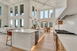 Kitchen featuring decorative light fixtures, wall chimney exhaust hood, light wood-type flooring, white cabinets, and stainless steel appliances