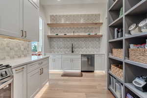 Kitchen featuring white cabinets, tasteful backsplash, appliances with stainless steel finishes, light wood-style floors, and open shelves