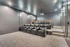 Carpeted cinema room featuring a textured ceiling and baseboards