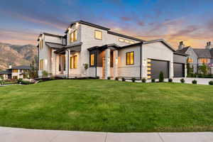 Contemporary home with stone siding, a lawn, an attached garage, concrete driveway, and a standing seam roof