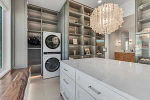 Laundry area featuring stacked washer and clothes dryer and a chandelier