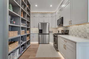 Kitchen featuring appliances with stainless steel finishes, decorative backsplash, light wood-type flooring, light stone countertops, and recessed lighting