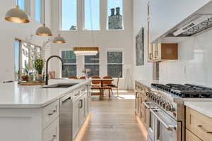 Kitchen with appliances with stainless steel finishes, hanging light fixtures, a high ceiling, light stone countertops, and an island with sink