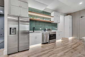 Kitchen with appliances with stainless steel finishes, open shelves, white cabinetry, and decorative backsplash
