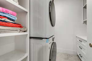 Laundry area featuring stacked washer / drying machine and light tile patterned flooring