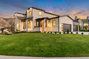 View of front of home with stone siding, a lawn, a garage, driveway, and a standing seam roof