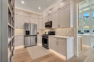 Kitchen with stainless steel appliances, decorative backsplash, light wood-type flooring, light stone counters, and recessed lighting