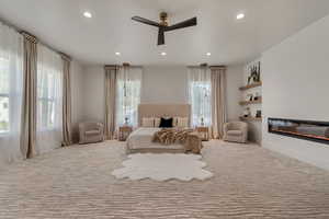 Carpeted bedroom featuring a glass covered fireplace, ceiling fan, and recessed lighting