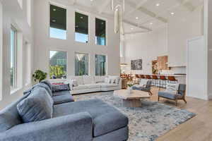 Living room featuring light wood finished floors, beamed ceiling, coffered ceiling, recessed lighting, and a high ceiling