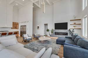 Living area featuring light wood-style flooring, beamed ceiling, a fireplace, a high ceiling, and coffered ceiling