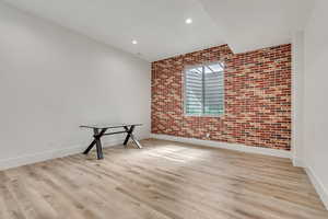Empty room with brick wall, light wood finished floors, and recessed lighting