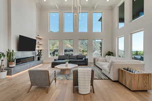 Living area with light wood finished floors, beamed ceiling, a premium fireplace, crown molding, and recessed lighting