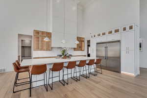 Kitchen with a large island with sink, a breakfast bar, decorative backsplash, built in refrigerator, and a towering ceiling