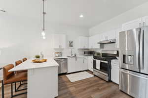 Kitchen with a counter-level peninsula, quartz countertops, stainless steel appliances, a breakfast bar and hanging light fixtures