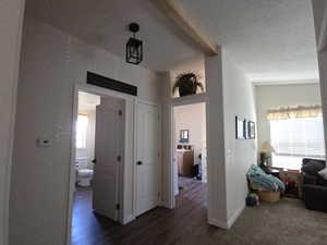 Corridor with dark wood finished floors, a textured ceiling, and beamed ceiling