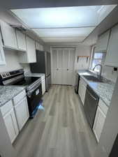 Kitchen with white cabinetry, stainless steel appliances, light wood-style floors, open shelves, and light stone counters