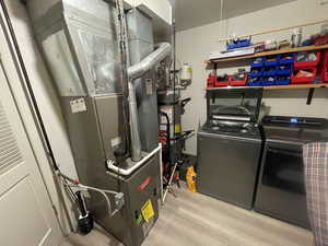 Washroom featuring light wood-type flooring, heating unit, separate washer and dryer, and water heater