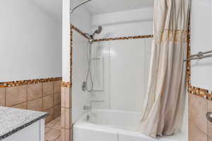 Bathroom with tile walls, shower / bath combination with curtain, vanity, a wainscoted wall, and tile patterned flooring